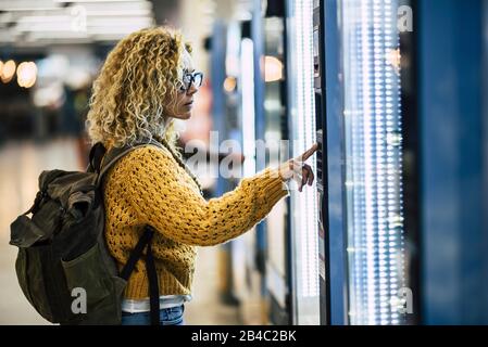 Alone traveler caucasian beautiful woman at the airport or. station choosing and buying food from automatic machine - concept of travel lifestyle for independent people enjoying life Stock Photo