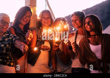 New year eve celebration with group of mixed ages and generations women having fun with sparklers outdoor - people having fun together in friendship - dark evening time and party activity Stock Photo