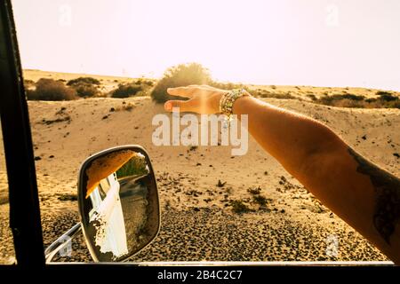 Travel and freedom concept for alternative lifestyle people - close up of hand of a caucasian woman outside the window of the vintage car playing with the wind while traveling - desert in background and sunlight Stock Photo