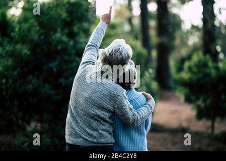 Couple of mature senior old people hug and enjoy the outdoor leisure activity together in the forest - green trees in background - unrecognizable man and woman for elderly healthy ilfestyle