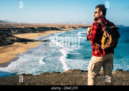 Standing man traveler people look and enjoy the destination on a wonderful tropical beach with rock cliff - alternative vacation lifestyle - wanderlust and backpack life Stock Photo