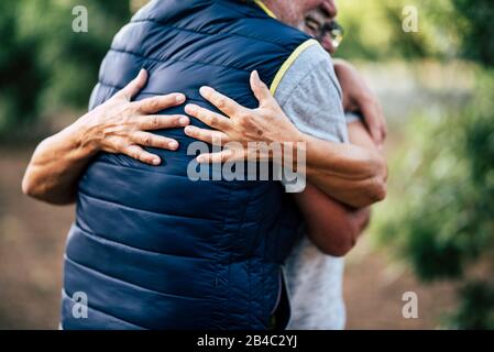 Concept of love with no limit age - couple of unrecognizable senior mature people hug and touch together with care in outdoor leisure activity with defocused green forest in background Stock Photo