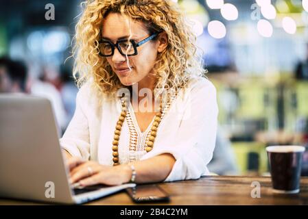 Modern adult caucasian woman working on a laptop computer at her worlplace desktop - people at work with technology concept - internet connection and defocused background Stock Photo