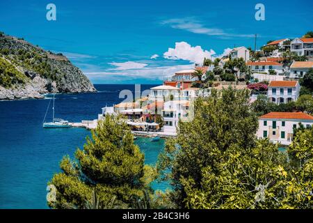 Assos village. Beautiful view to vivid colorful houses near blue turquoise colored transparent bay lagoon with yacht ship. Kefalonia, Greece. Stock Photo