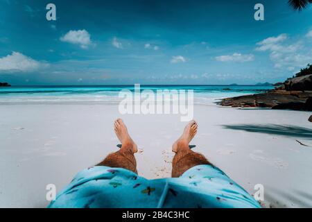 Travel vacation background male legs with swim short on paradise white sand tropical beach in front of turquoise sea. Exotic holidays. Stock Photo