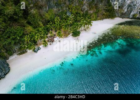 Aerial drone view of abandoned house hut on Pinagbuyutan Island in El Nido. Amazing white sand beach and emerald lagoon water. Stock Photo