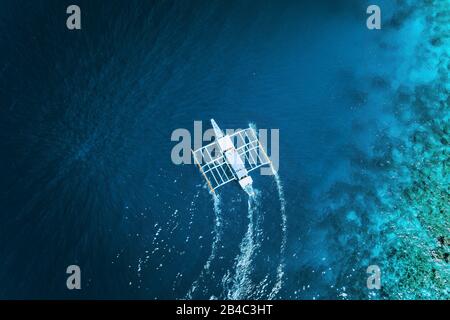 Aerial drone view of white traditional Filipino boat floating on top of clear blue water surface. El Nido, Palawan, Philippines. Stock Photo