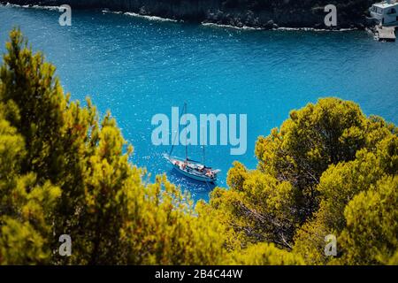 White yacht take a shelter in beautiful blue lagoon of Assos village Kefalonia. Frame between top of the green pine trees. Greece. Stock Photo