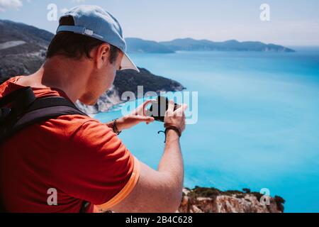 Man capture photograph of myrtos coastline sea landscape. Blue cyan water surface with island shape, Kefalonia, Greece. Stock Photo