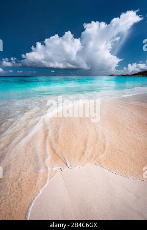 Ocen wave rolling towards tropical sandy beach. Turquoise blue ocean in background with white clouds above. Grand Anse, Seychelles. Stock Photo