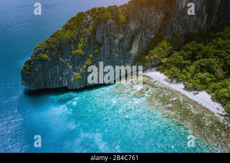 Aerial drone view of tropical beach with banca boats on Entalula Island. Karst limestone rocky mountains surrouns blue bay with beautiful coral reef. Stock Photo