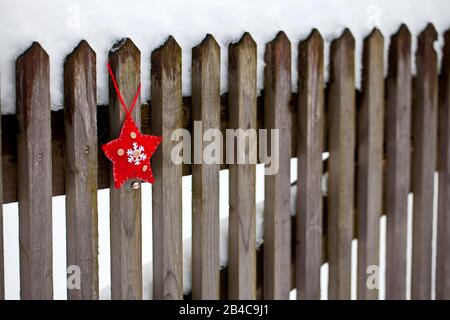winterly Christmas scenery with red white felt star ornament hanging from snow covered wooden fence Stock Photo