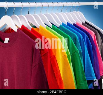 row of many fresh new fabric cotton t-shirts in colorful rainbow colors hangng on clothes rail in wrdrobe. Various colored shirts on blue white backgr Stock Photo