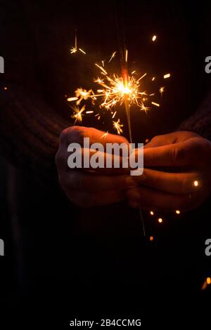Christmas and new year eve concept image with close up of a pair of man hands taking a red fire sparkler to celebrate the night party - focus on fireworks and hope for people future Stock Photo