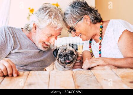 People and dog concept with couple of happy couple of senior mature man and woman smiling and having fun with their little puppy pug  - concept of animal therapy and happiness Stock Photo