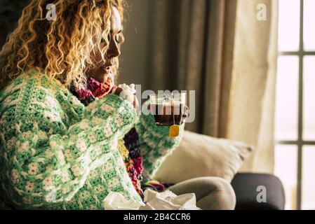 Adult beautiful caucasian woman at home sick with ill and cold drinking  hot tea - fever and seasonal influenza illness concept for unhealthy people sitting and taking medicine Stock Photo