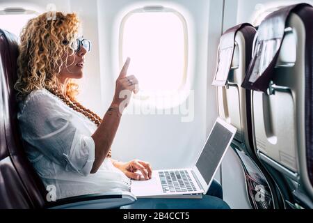 Beautiful female passeger of airplane use personal laptop computer on board with wifi internet connection and ask for hostess help - travel for business modern people concept Stock Photo