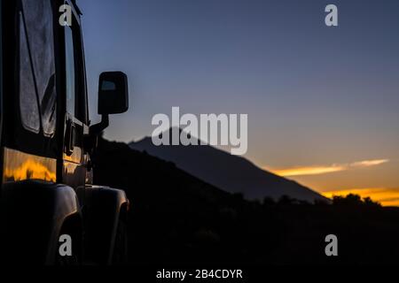 Close up of black of roas adventure car parked with beautiful sunset and mountain in background - concept of travel and discover wild places and enjoy alternative vacation adventure lifestyle Stock Photo