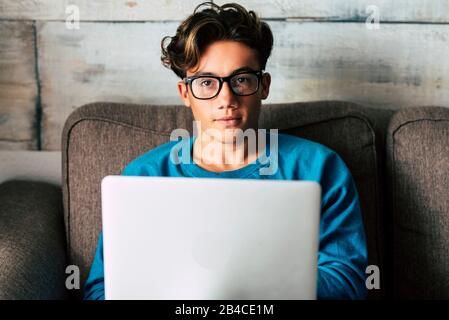Portrait of handsome caucasian people teenager working with personal laptop computer at home sitting on the sofa - concept of student for high school or graduate or job search with modern technology Stock Photo