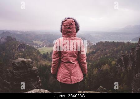 Junge Frau in winterlicher Kleidung im Freien, die allein auf einem Berg steht und die Aussicht genießt, Reiselebensstil-Harmoniekonzept, Rückansicht Stock Photo