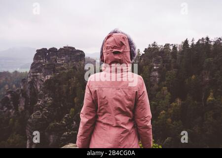 Junge Frau in winterlicher Kleidung im Freien, die allein auf einem Berg steht und die Aussicht genießt, Reiselebensstil-Harmoniekonzept, Rückansicht Stock Photo