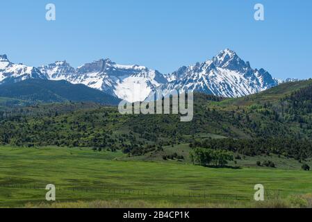 Landscape of green meadow, and hillside with the Sneffels Mountain Range in the background near Ridgway and Telluride, in Colorado Stock Photo