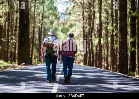 Travel lifestyle for old senior couple walking together in the middle of the road with high trees forest on both sides - lifestyle and togetherness forever life concept - aged people Stock Photo