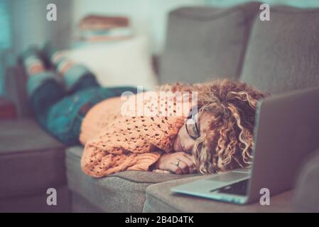 Young woman with laptop at home, lay down on the sofa and sleeping - people with modern technology device to connect and search the internet web media