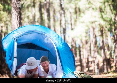 Happy retired senior caucasian couple enjoying the outdoor leisure activity together lay down relaxing inside a camping tent in the free nature forest - happiness for old active people Stock Photo