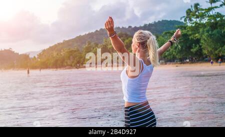 Blonde young woman puts her arms out and looks at the sunset, Ao Nang Beach, Krabi, Thailand Stock Photo