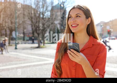 Front view portrait of a confident Brazilian woman holding mobile phone looking to the side in city street Stock Photo