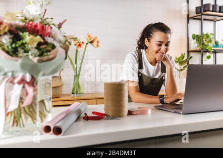 Smiling flower shop owner using laptop computer. Female florist working on laptop at counter. Stock Photo