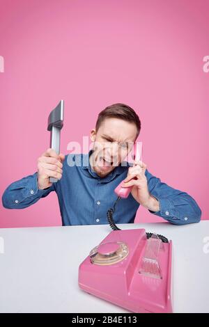 Furious young man with axe expressing rage while shouting in pink plastic telephone receiver and complaining about something Stock Photo