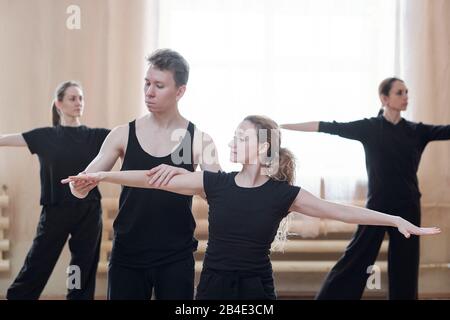 Young male instructor of dancing helping one of females with outstretched arms during training in modern studio Stock Photo
