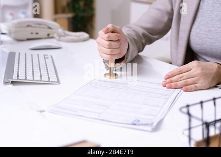 Hands of young female office worker sitting by desk and putting seal on financial document before sending it to client Stock Photo