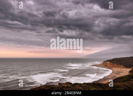 Black clouds over a bay on the Great Ocean Road at Aireys Inlet. On the horizon, the sunset can be guessed Stock Photo