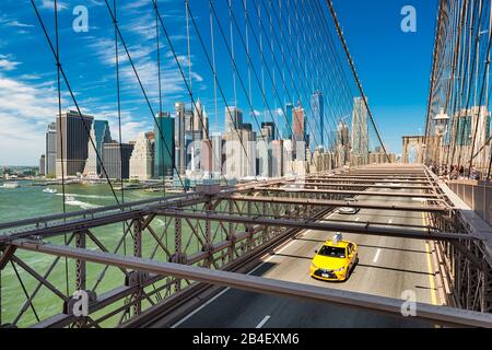 Iconic yellow taxi on the Brooklyn Bridge with the Manhattan skyline in the background, New York Stock Photo