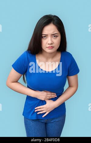 Young chinese woman standing isolated on grey background coronavirus concept holding belly having stomachache looking camera serious Stock Photo