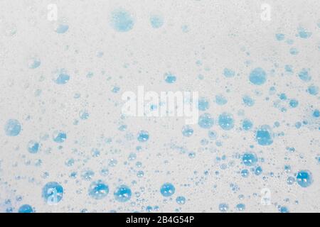 White foam with bubbles popping in blue water. Stock Photo