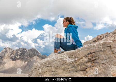 Junge Frau sitzt auf Felsen, Zugspitzplatt, Zugspitze, Garmisch-Partenkirchen, Wettersteingebirge, Alpen, Oberbayern, Bayern, Deutschland, Europa Stock Photo