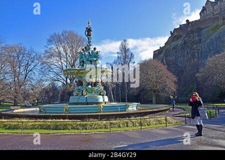 Two female tourists take selfies on cellphones in front of Ross Fountain and Edinburgh Castle in Princes Street Gardens, Edinburgh, Scotland, UK Stock Photo
