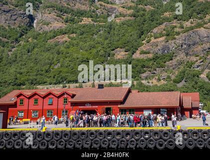 Flåm, tourists at the TICKETS & VISITOR CENTER, red wooden house, pier for ships, rock faces, trees, Sogn og Fjordane, Norway, Scandinavia, Europe Stock Photo