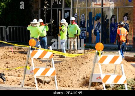 Road construction workmen wearing bright flourescent apparel work on the sidewalk edging stones on a road expansion project in Tuscon AZ Stock Photo