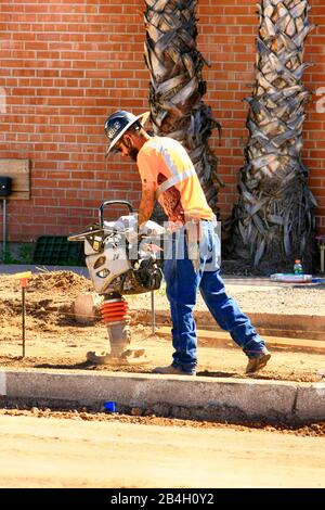 Workman using a vibrating compactor machine on the new sidewalk area of a road expansion project in Tucson AZ Stock Photo