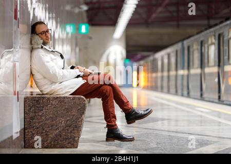 Crying man with feels unhappy and depressed, looking down, receiving bad message, holding smartphone,  on empty subway station. Emotional crisis, trou Stock Photo