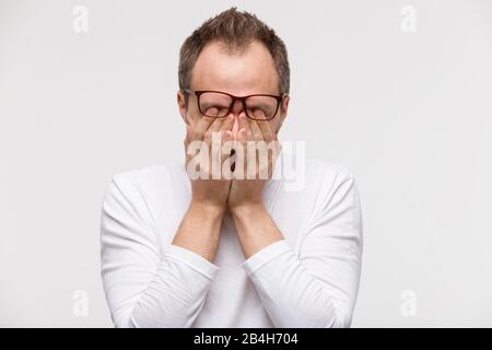Sleepy man in eyeglasses rubbing her eyes, feels tired after working on laptop, isolated on white background. Overwork, exhausted, chronic fatigue, me Stock Photo