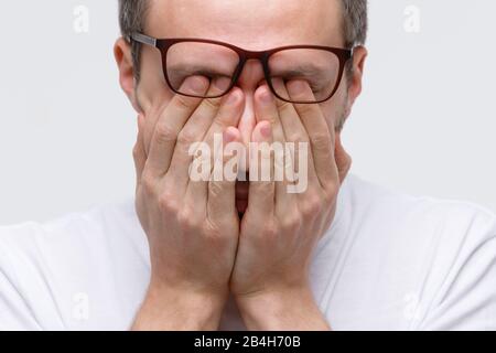 Sleepy man in eyeglasses rubbing her eyes, feels tired after working on laptop, isolated on white background. Overwork, exhausted, chronic fatigue, me Stock Photo