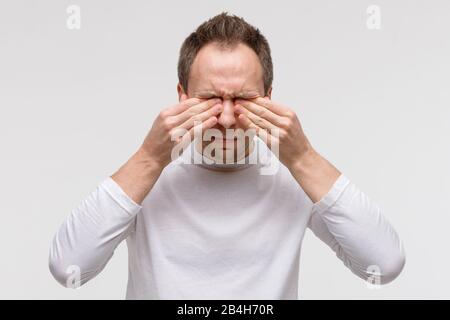 Close up of man has a problem with contact lenses, rubbing his swollen eyes due to pollen, dust allergy. Dry eye syndrome, watery, itching. Isolated o Stock Photo