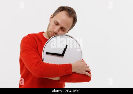 Studio portrait of tired man fell asleep with a round clock, holding in his hands, isolated on white background. Chronic lack of sleep, insomnia, phys Stock Photo