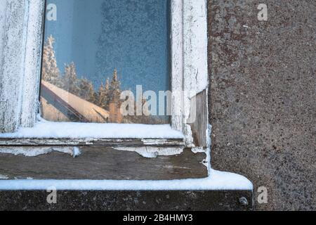 Schneebedeckte, alte Fensterscheibe mit Eisblumen und Spiegelung einer sonnigen, winterlichen Landschaft und Hütte in grauer Fassade in den Vogesen, F Stock Photo